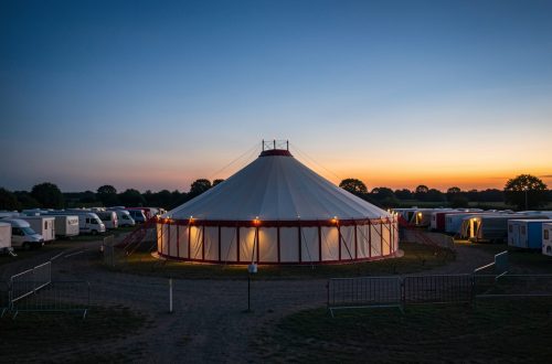 Chapiteau de cirque itinérant installé dans un terrain calme au crépuscule, entouré de caravanes et d’équipements soigneusement entretenus.